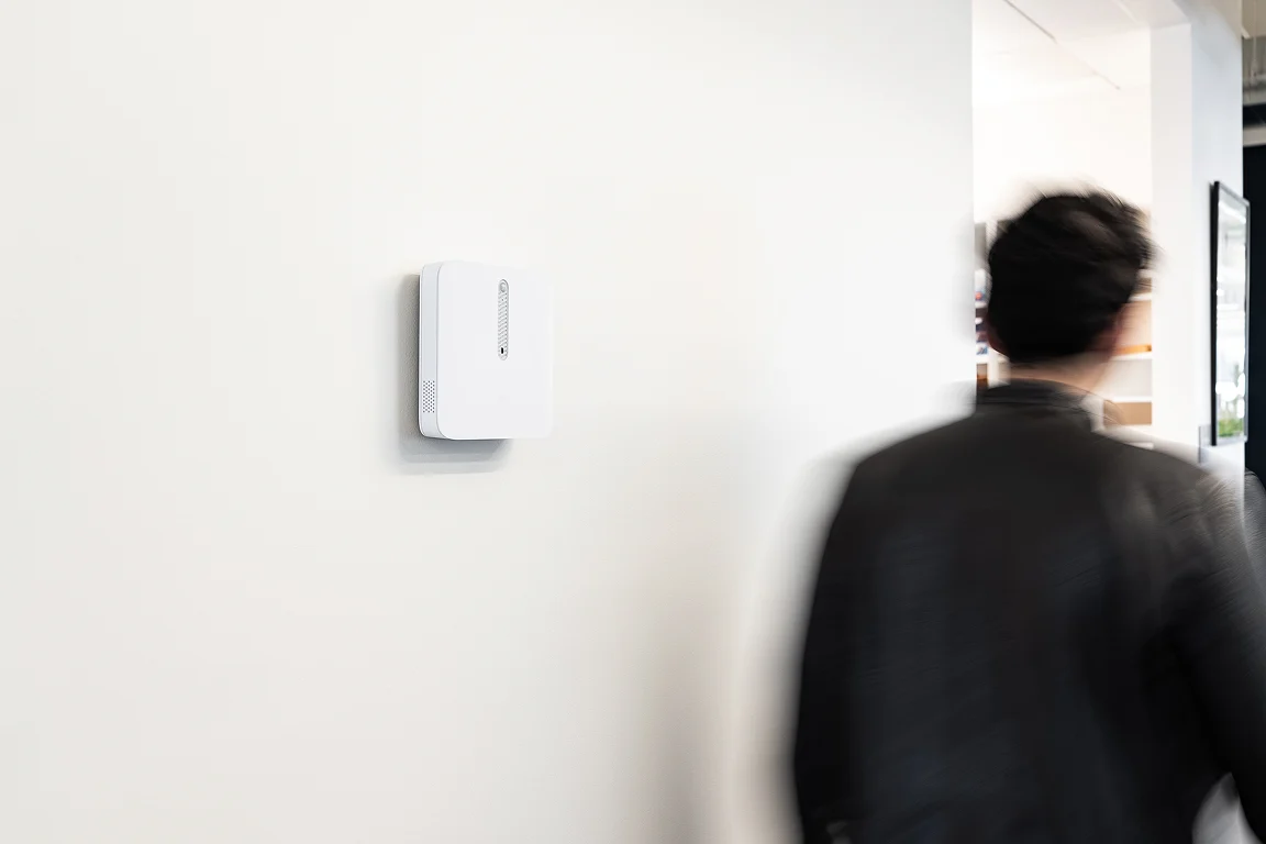 Capteur d’ambiance Verkada fixé au mur d’un couloir de bureaux, une personne passant devant